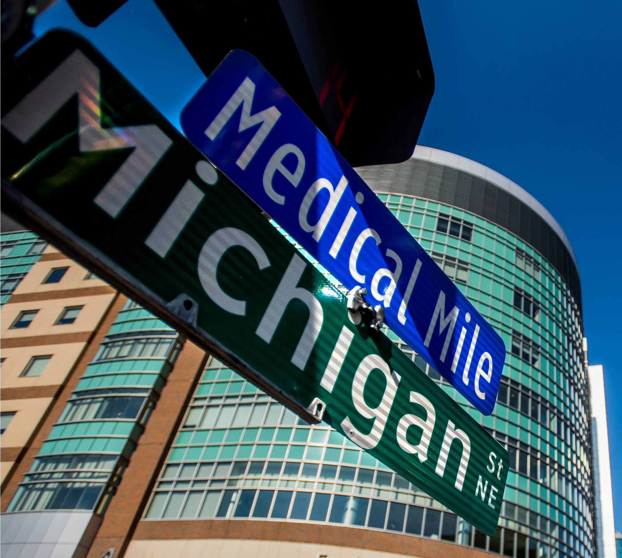Close up photo street signs listing "Michigan Street NE" and "Medical Mile", with a medical building in the distance.